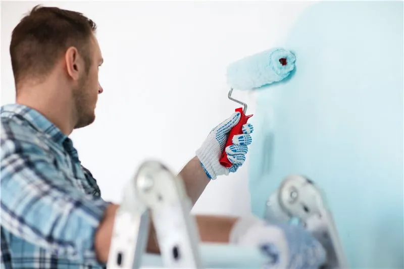 Man painting a kitchen wall during a kitchen cabinet update and painting.